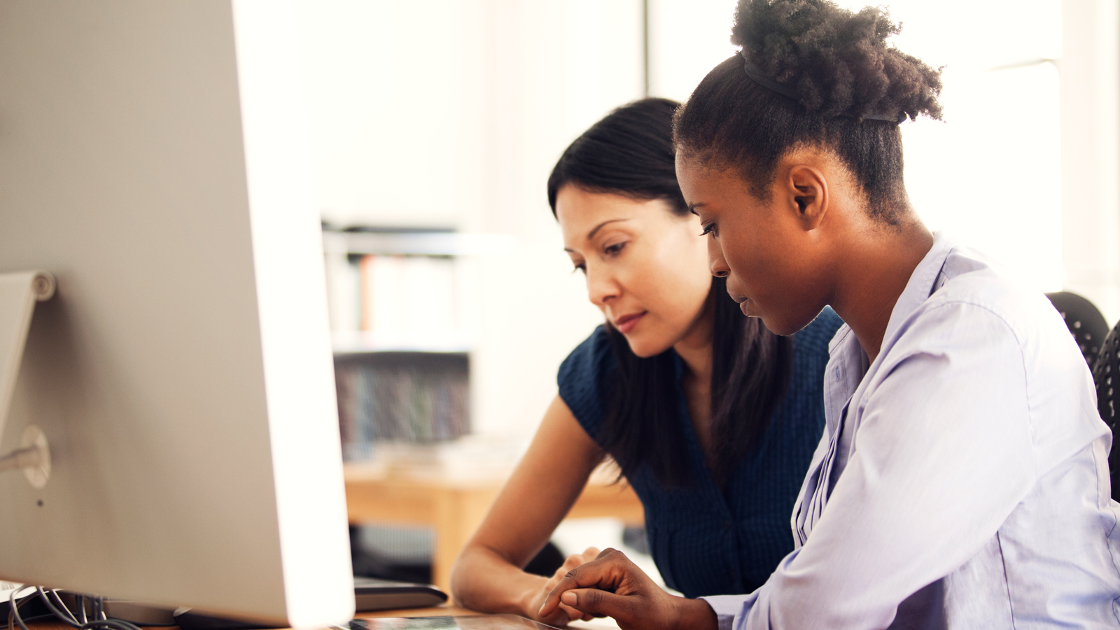 businesswomen-1600x900 Two women sit in front of a computer and discuss content on screen.
