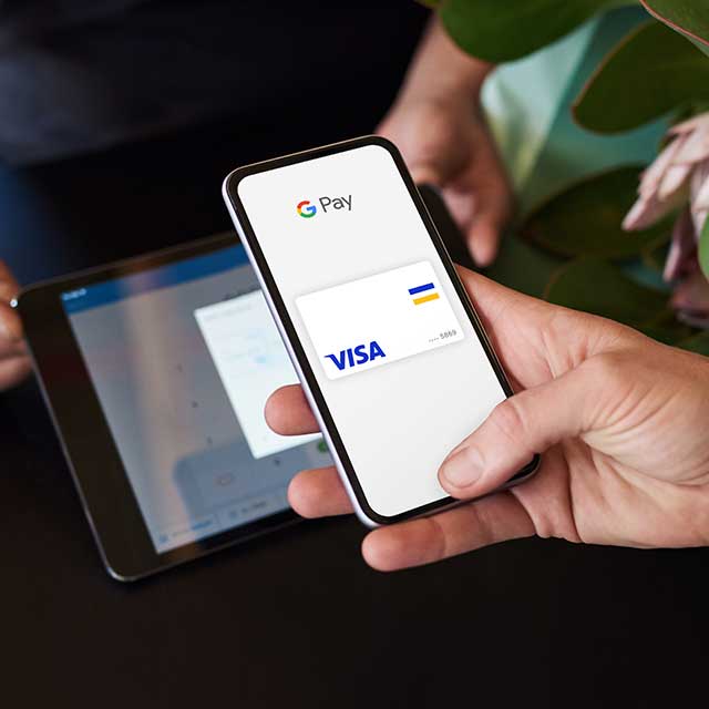 A person holding his phone in front of a tablet ready to pay with Google Pay. 