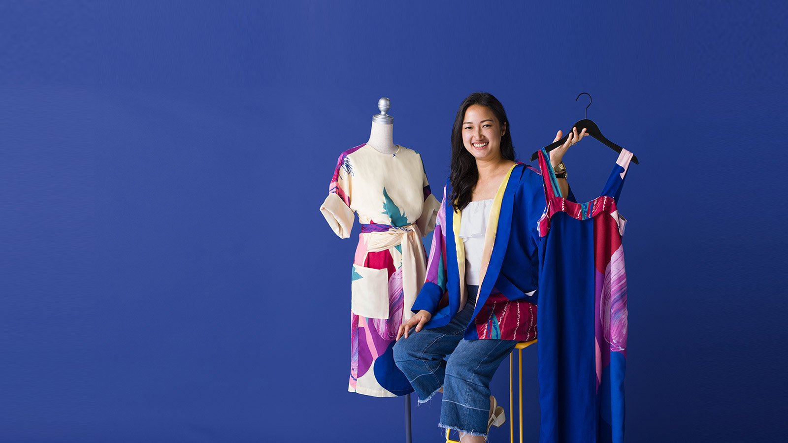 A woman posing next to a dress while seated on a chair, advertising an ecommerce starter kit for fashion entrepreneurs. 