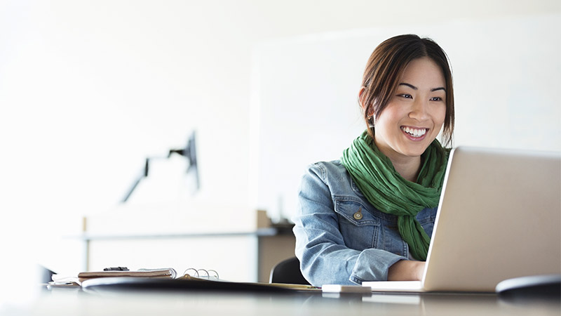 A female entrepreneur smiles while working on her laptop computer at the Visa small business hub. 